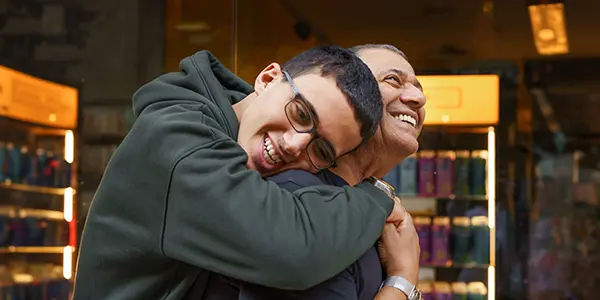 Smiling Teenage Boy Embracing Grandfather Amidst the Bustle of a Shopping Center