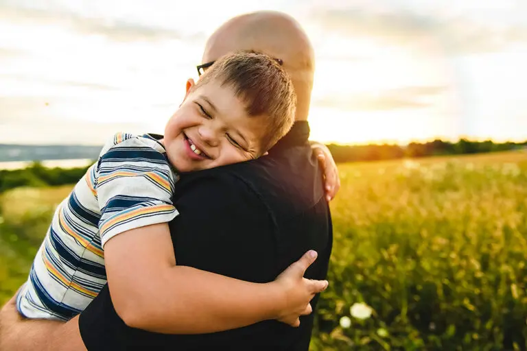 little boy with down syndrome in sunset on summer season hugging his father