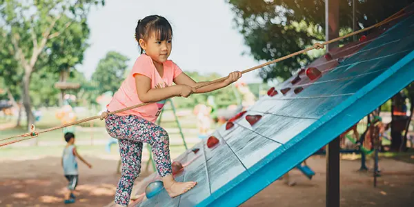 girl using rope to climb on climbing wall at park