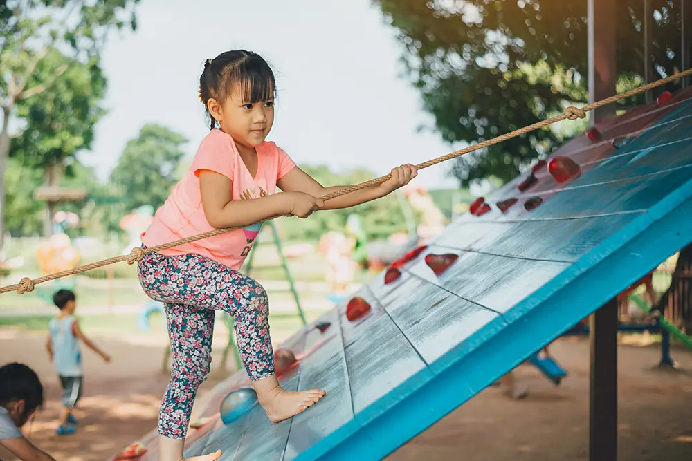 girl using rope to climb on climbing wall at park